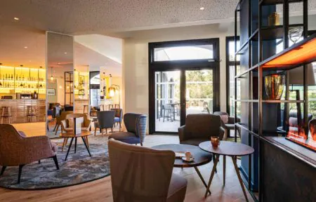 en::Lounge area of the bar with a central shelving unit and fireplace, double doors opening onto the outdoor terrace. fr::Espace lounge du bar avec meuble central et cheminée, double ouverture sur la terrasse extérieure.