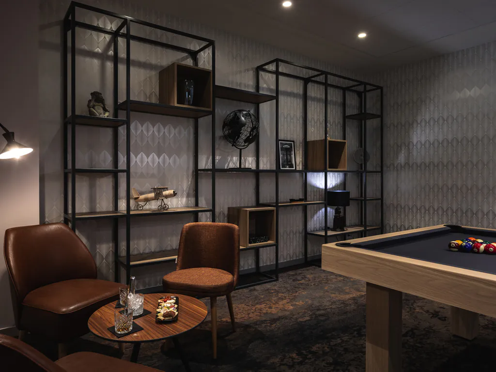 en::Wooden billiard table in an elegant room, grey walls, long wall shelf with decorative objects, leather armchairs and glasses with snacks. fr::Billard en bois dans une salle élégante, murs gris, étagère murale avec objets décoratifs, fauteuils en cuir et verres avec amuse-bouche.