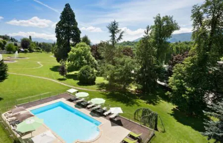 en::Outdoor pool in a landscaped park with a solarium area. fr::Piscine extérieure au cœur d’un parc arboré avec espace solarium.