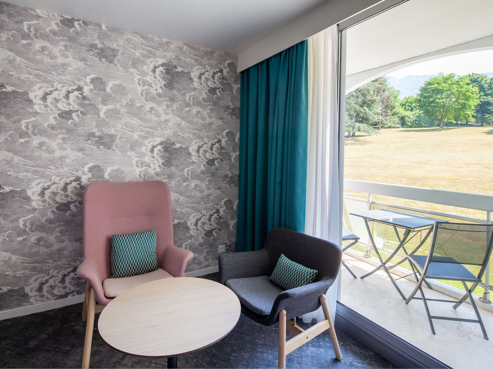 en::Pink and grey chair with cushion near a coffee table, large bay window opening onto a terrace with outdoor furniture facing the park. fr::Chaise rose et grise avec coussin près d’une table basse, grande baie vitrée ouvrant sur une terrasse aménagée face au parc.