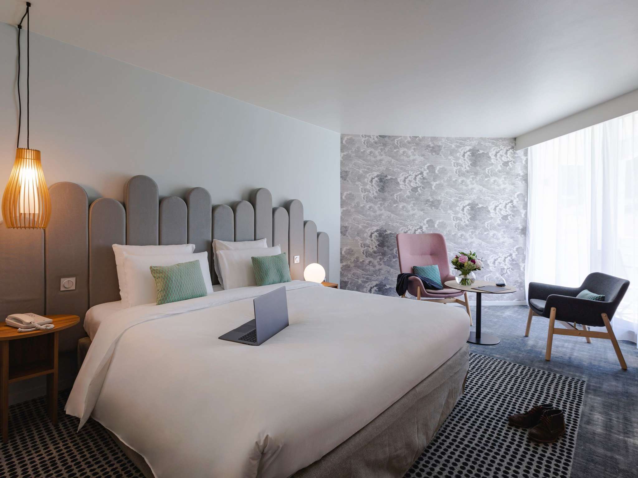 en::Room in grey and pastel tones with a large bed, lounge area near a bay window behind fr::Chambre aux tons gris et pastel avec grand lit, espace salon devant une baie vitrée avec voilage.