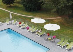 en::Outdoor pool with blue water, wooden deck, sun loungers and parasols, set in a park. fr::Piscine extérieure au fond bleu, terrasse en bois, transats et parasols au cœur d’un parc.
