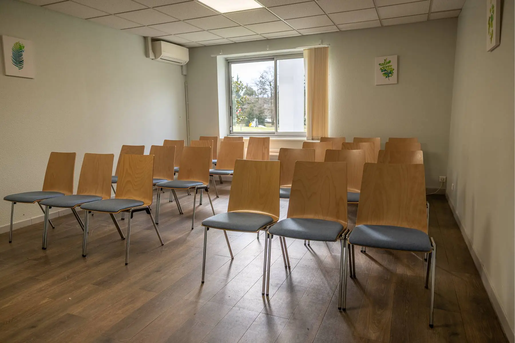 en::Two rows of chairs in a room, glass door with cream vertical blinds.fr::Deux rangées de chaises dans une salle, porte-fenêtre avec stores à lamelles jaune écru.