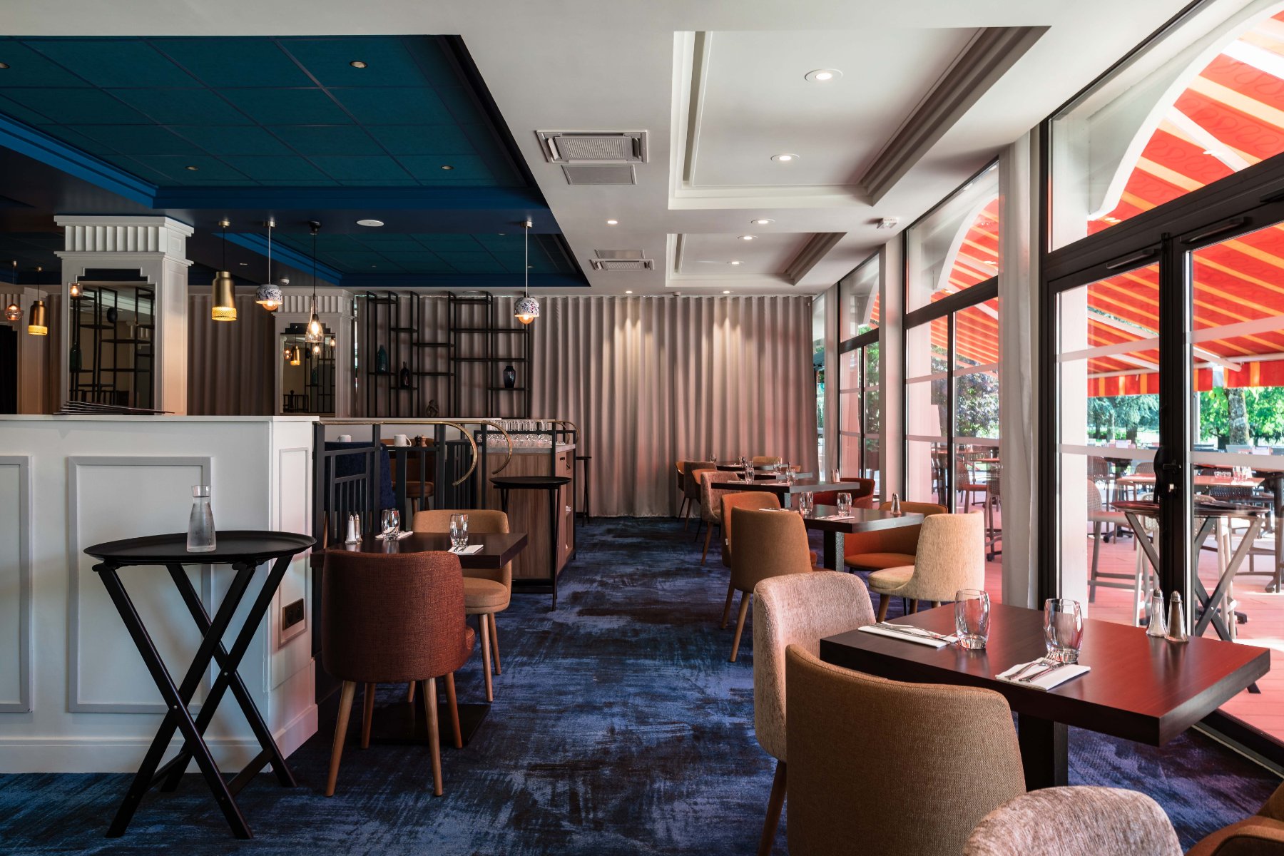 en::Set tables with glasses and cutlery along a bay window opening onto the terrace. fr::Tables dressées avec verres et couverts le long d’une baie vitrée ouvrant sur la terrasse.