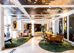 en::Hotel reception area with decorative tapestry on the ceiling and walls, depicting landscapes and exotic animals such as parrots, geese, and horses. fr::Réception de l’hôtel avec tapisserie décorative au plafond et sur les murs, représentant des paysages et animaux exotiques comme des perroquets, oies et chevaux.