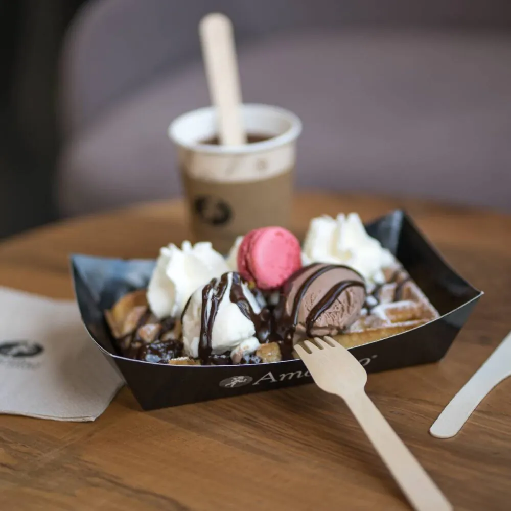 en::Amorino tray with waffle, ice cream, macaron and whipped cream, served with a coffee on a wooden coffee table in the tea room. fr::Barquette Amorino avec gaufre, boules de glace, macaron et chantilly, accompagnée d’un café, posée sur une table basse en bois du salon de thé.