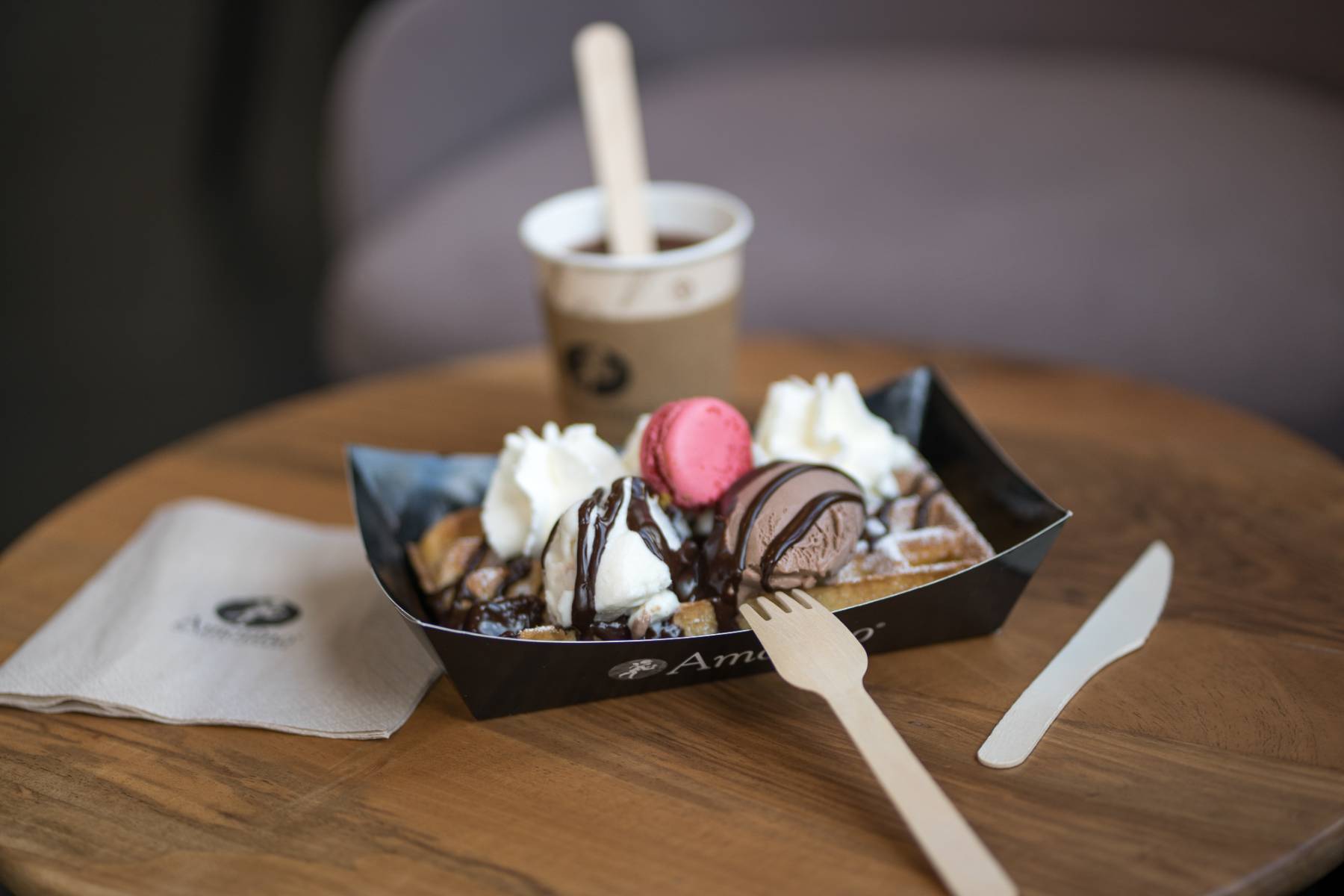 en::Amorino tray with waffle, ice cream, macaron and whipped cream, served with a coffee on a wooden coffee table in the tea room. fr::Barquette Amorino avec gaufre, boules de glace, macaron et chantilly, accompagnée d’un café, posée sur une table basse en bois du salon de thé.
