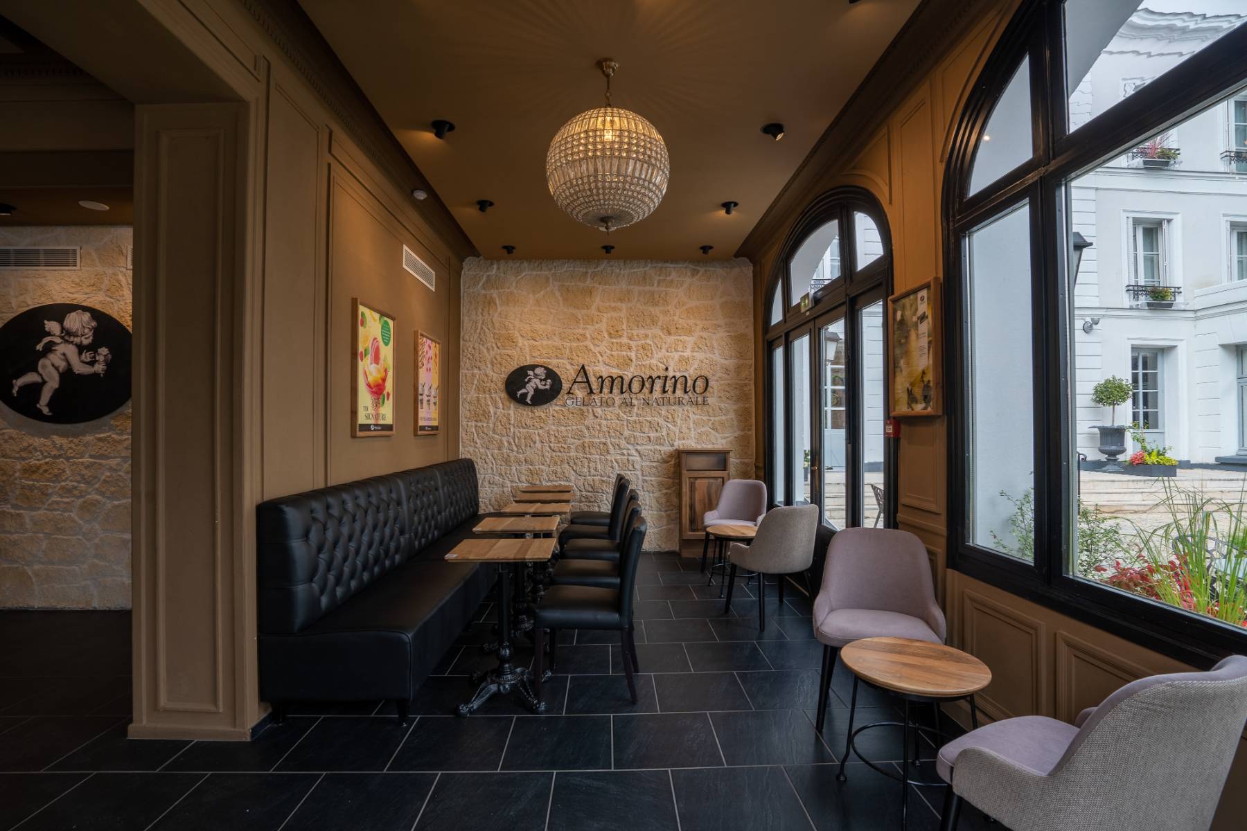en::Leather sofas along a wall, square tables and black chairs opposite, with a view over the hotel’s inner courtyard. fr::Canapés en cuir le long d’un mur, tables carrées et chaises noires en face, avec vue sur la cour intérieure de l’hôtel.