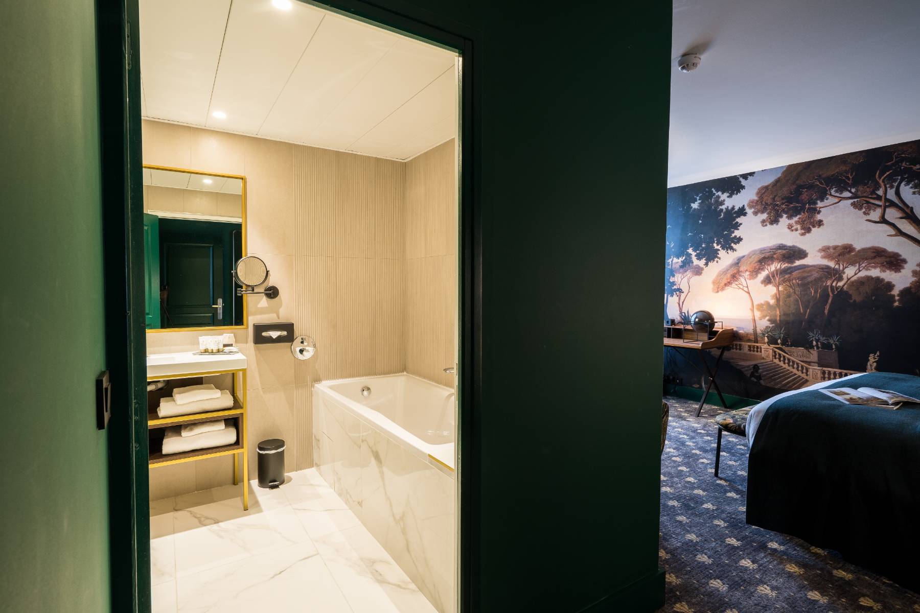 en::Bathroom with marble-effect tiles around the bathtub and on the floor, bedroom with an open book on the bed and a view of a tapestry depicting an old staircase surrounded by a large garden. fr::Salle de bain avec carrelage effet marbre autour de la baignoire et au sol, chambre avec livre ouvert sur le lit et vue sur une tapisserie représentant un escalier ancien entouré d’un vaste jardin.