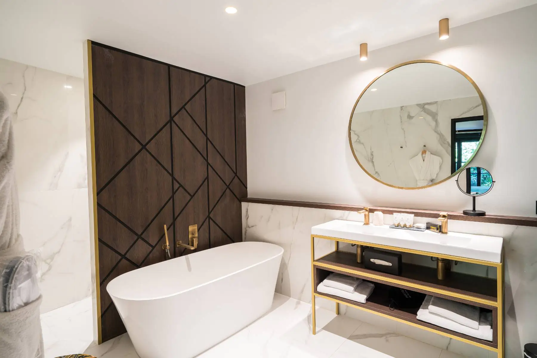 en::Bathroom combining wood, marble and brass, with outdoor greenery reflected in the main mirror and magnifying mirror. fr::Salle de bain mêlant bois, marbre et laiton, avec vue sur la végétation extérieure reflétée dans le miroir central et le miroir grossissant.