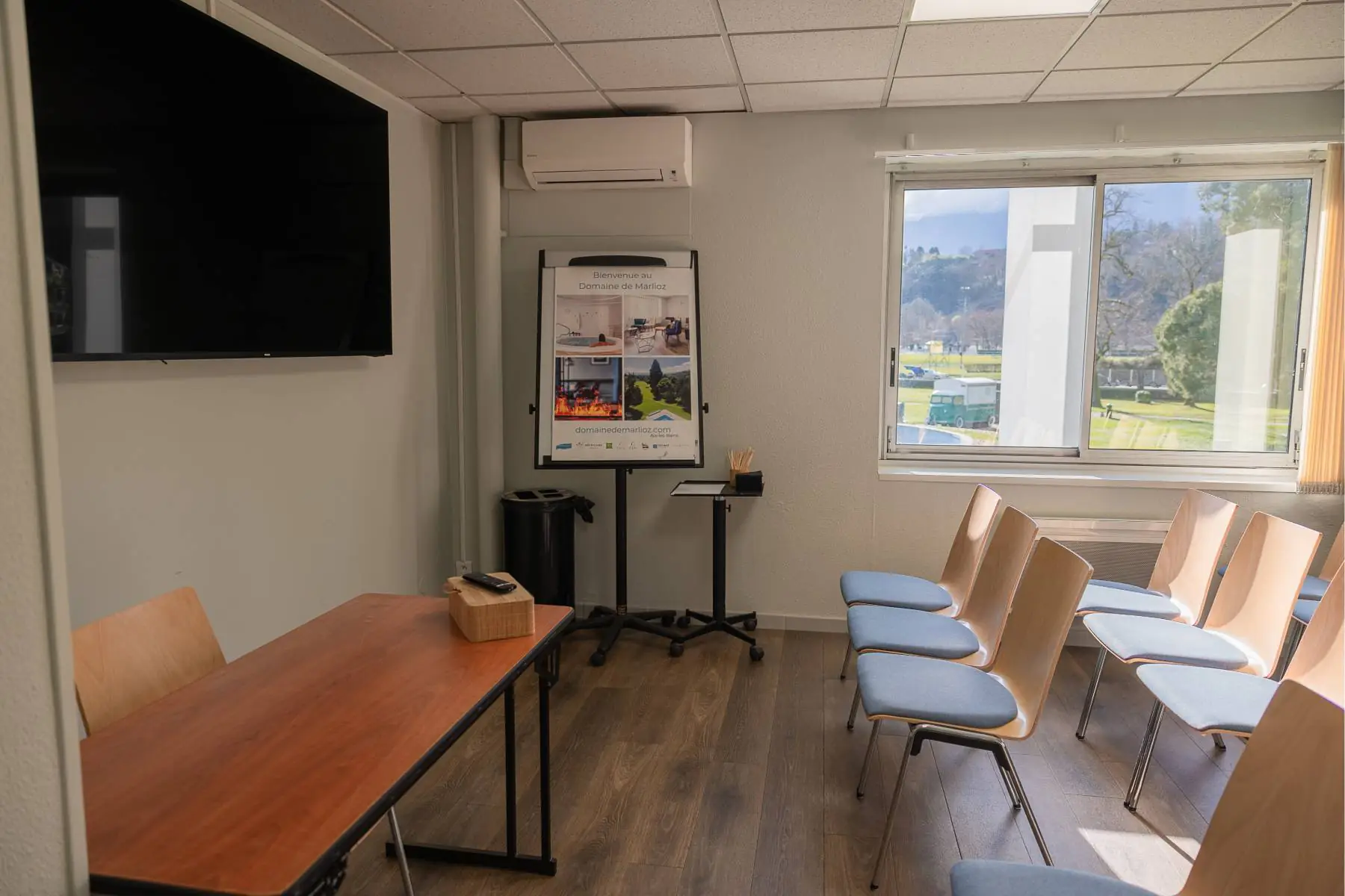 en:: Row of chairs facing a desk and screen, flip chart with hotel information. fr::Rangée de chaises face à un bureau et un écran, paperboard avec informations de l’hôtel