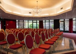 en::Meeting room under a glass roof, red theatre-style chairs, chandelier on. fr::Salle de réunion sous verrière, chaises rouges en théâtre, lustre allumé.