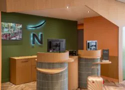 Novotel reception with wood counters, olive-green walls and backlit logo
