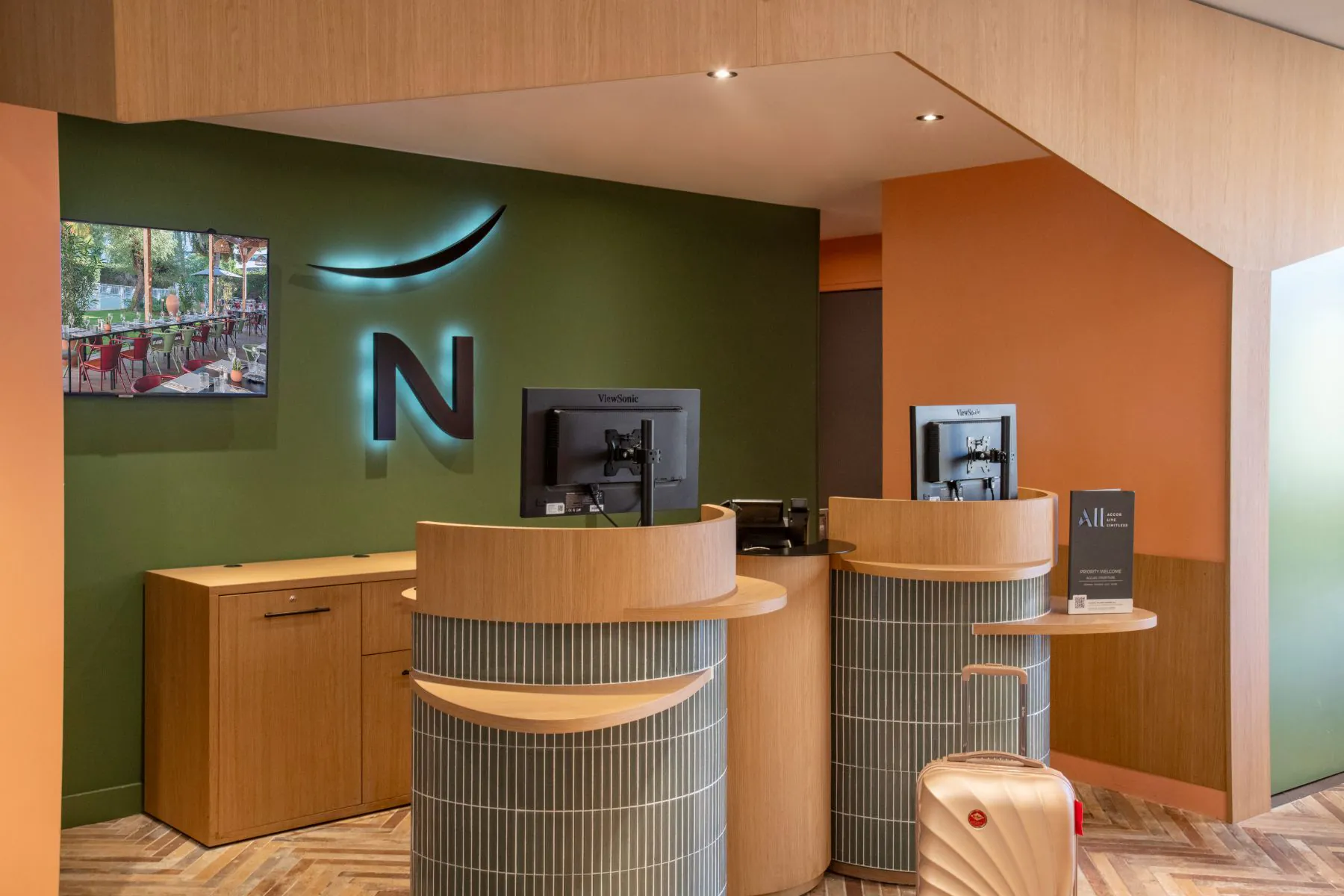 Réception Novotel avec comptoirs en bois, murs vert olive et logo rétroéclairé