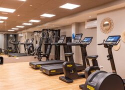 Une salle de fitness climatisée, avec larges miroirs et équipements complets : tapis de course, vélos et haltères