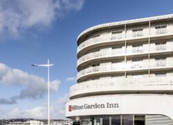 en::A white building with Hilton Garden Inn signage, alongside À l’Épicerie Restaurant Experience branding fr::Un bâtiment blanc avec une enseigne Hilton Garden Inn et une enseigne A l’Epicerie Restaurant Experience