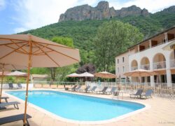 en::Blue swimming pool bordered by a tiled deck, with parasols and sun loungers, offering a view of the mountains. fr::Piscine aux eaux bleues bordée d’une plage carrelée, avec parasols et transats, offrant une vue sur les montagnes.