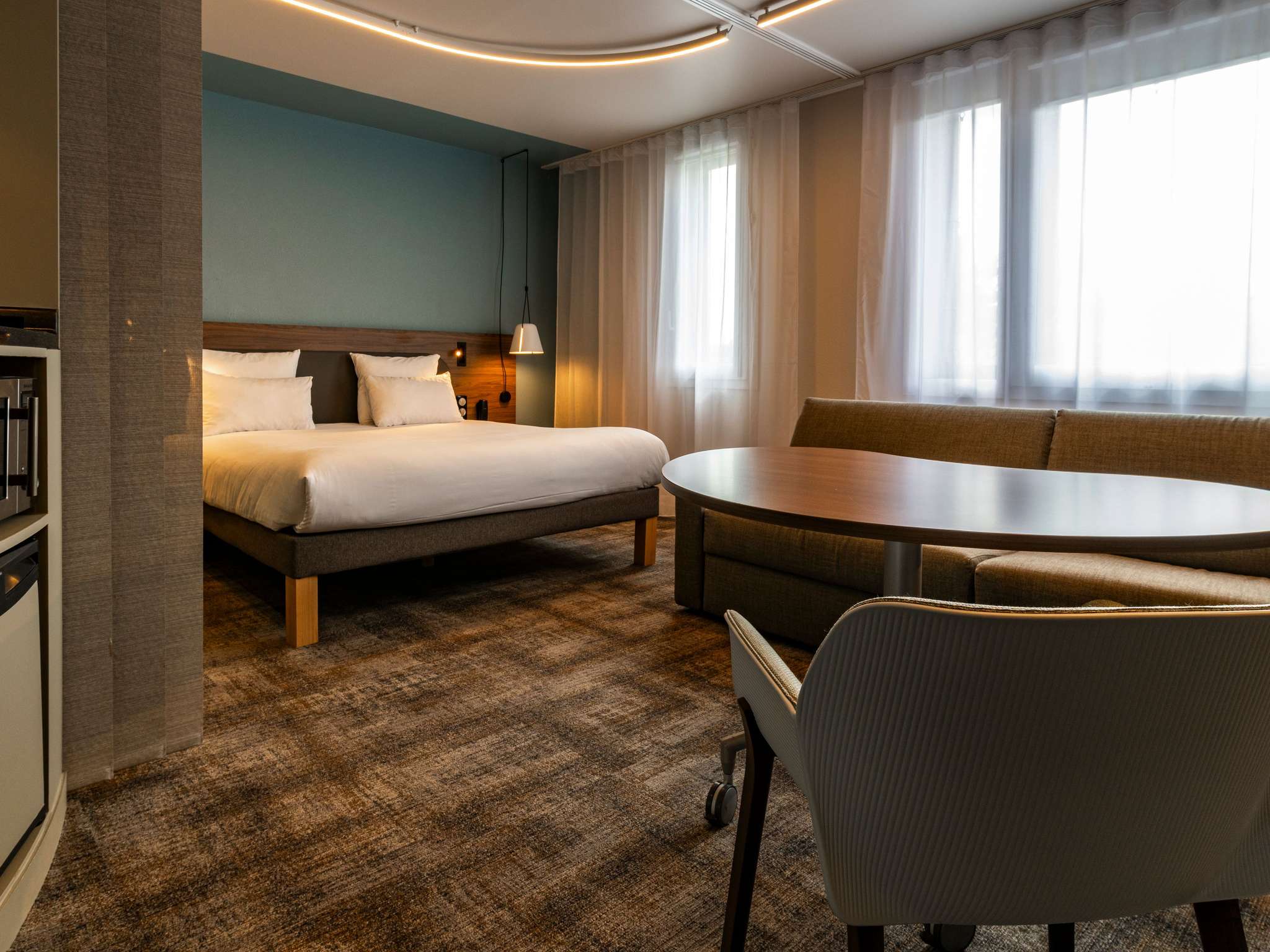 Suite with brown checkered carpet, red walls, a double bed and a two-person sofa bed in front of a wide dark wood table, with a stylish teal-blue wall.