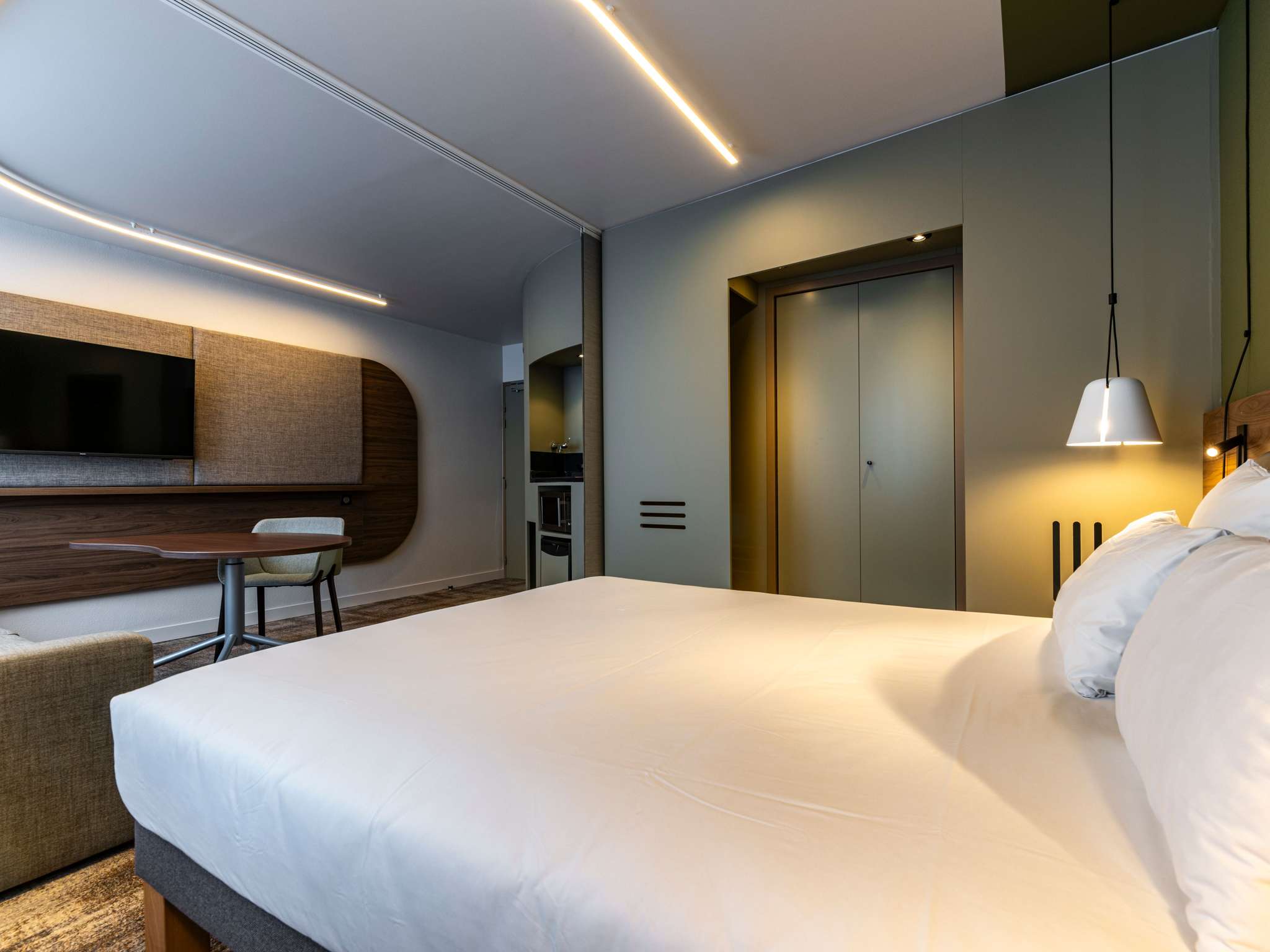 Double bed with a white pendant light and reading light on the wooden headboard. Opposite, a desk with a wall-mounted TV.