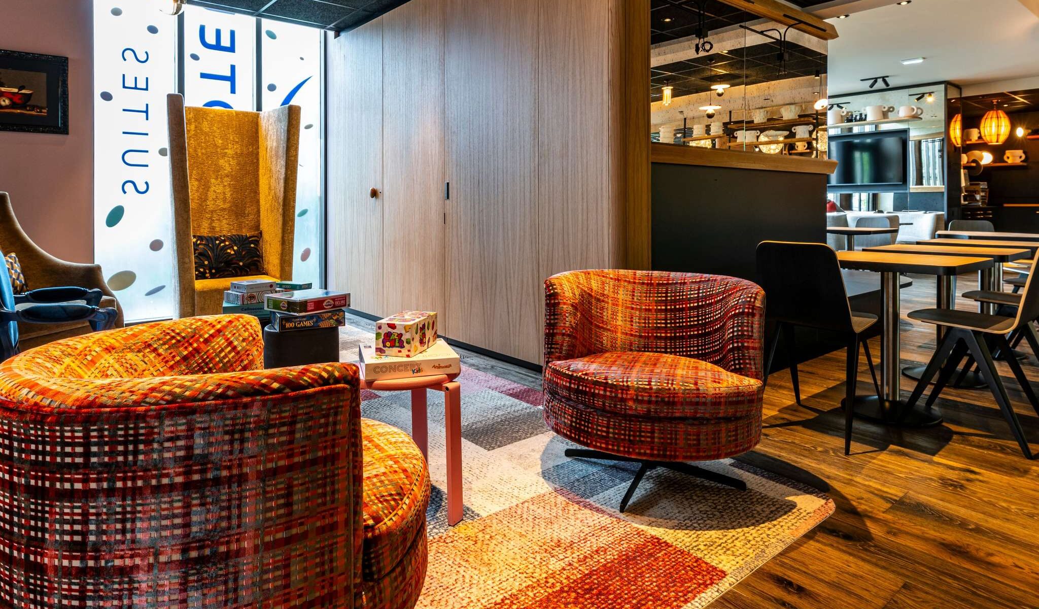 Adjacent to the lobby and bar area, a games corner with very colorful seating in various sizes and Novotel Suites stickers on the bay windows in the background.