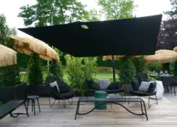 Un focus sur l'espace détente de la terrasse avec du mobilier de jardin en métal et coussins noirs et des parasols en paille.