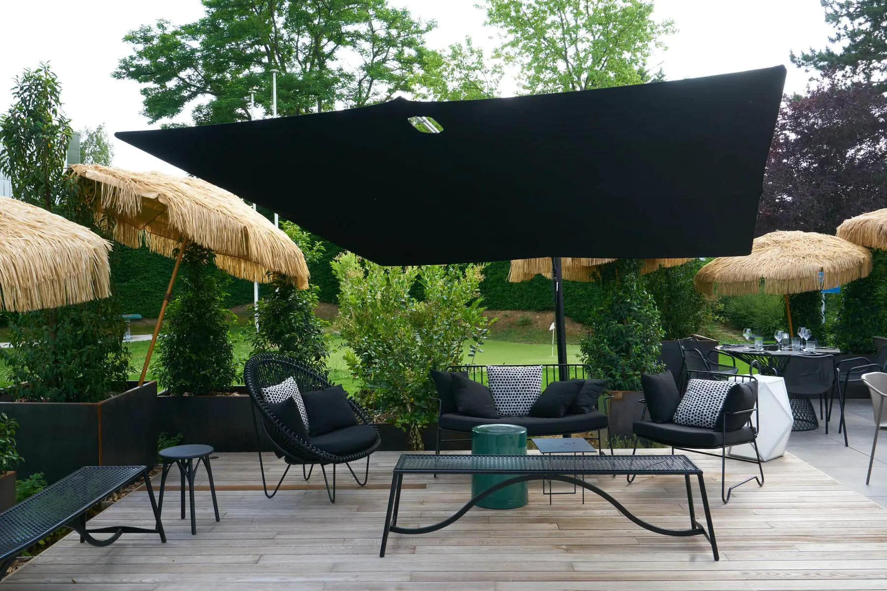 A close-up of the terrace relaxation area featuring metal garden furniture with black cushions and straw parasols.