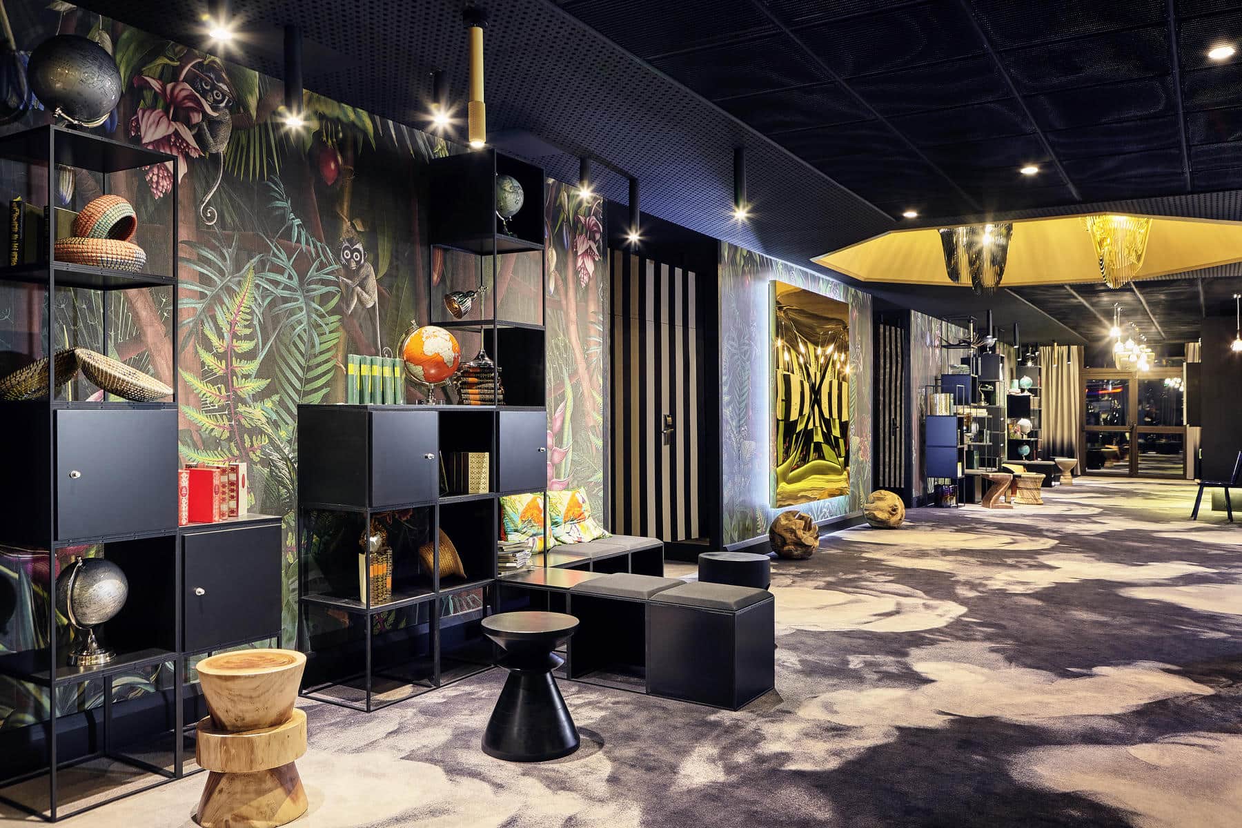 Close-up of one side of a vast, colourful reception hall with contemporary décor, featuring a black-and-white carpet, a black ceiling, modern black and light marble furniture, gold decorative elements, and sections of walls with black-and-white stripes alongside a tropical forest-inspired design.