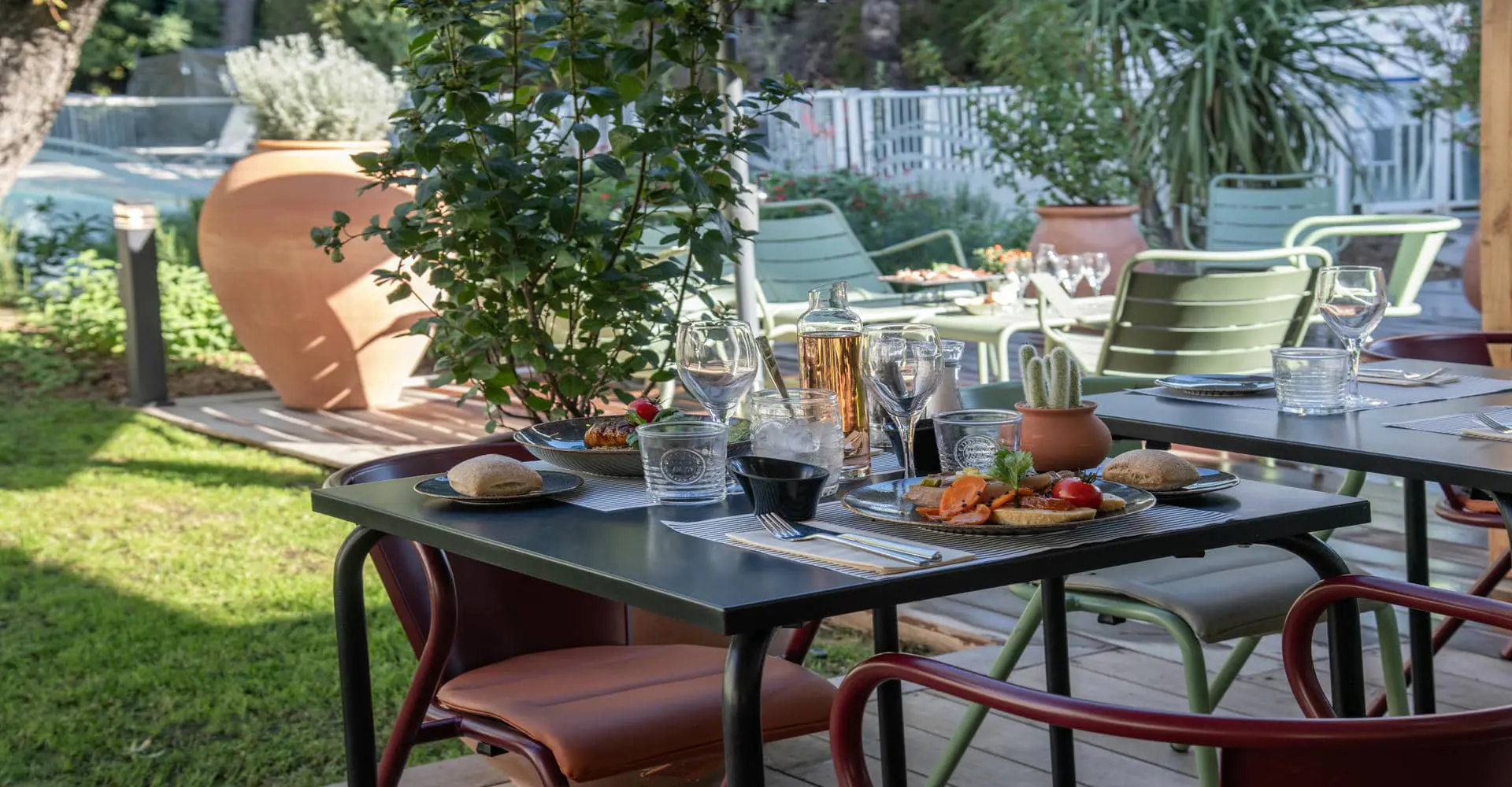 Un table dressée en extérieur pour deux personnes avec des plats colorés servis, une carafe remplie et un cactus en décoration.
