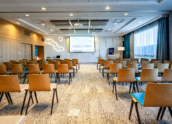 Grande salle de réunion avec au premier plan plusieurs rangées de fauteuils tournés vers un écran mural en arrière-plan.