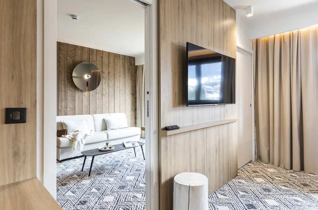 Vue depuis une pièce moquettée aux éléments muraux en bois sur un coin salon composé d’une banquette et d’une table basse.