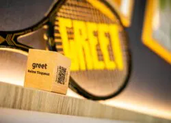 Dé avec « Greet Reims Tinqueux » écrit dessus, QR code « Besoin d’aide » et raquette de tennis avec « greet » en jaune, présentés sur des étagères en bois.