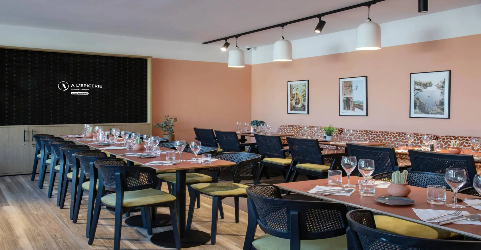 Vue d'une salle de restaurant avec chaises, banquettes et tables dressées, logo A l'Epicerie sur grand écran