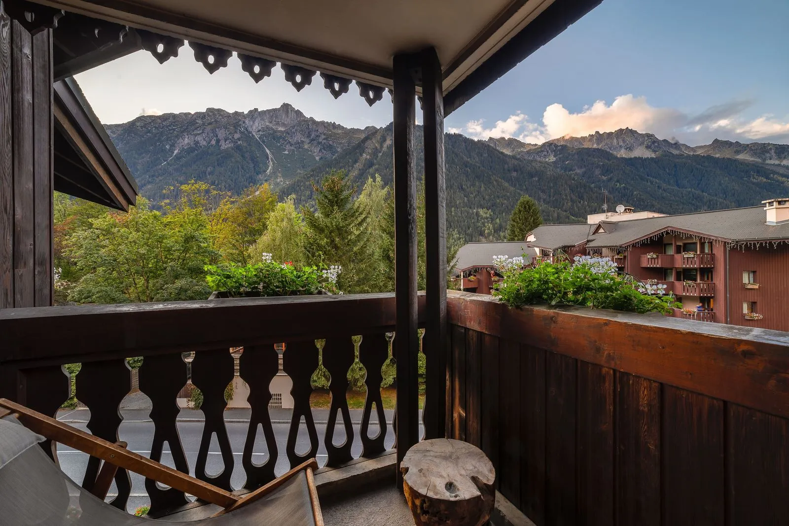 Vue depuis un balcon d’hébergement de groupe pour un séminaire à la montagne, avec garde-corps en bois et chaises longues au premier plan, surplombant des bâtiments hôteliers de style chalet à droite et des sommets montagneux boisés s’étendant à l’arrière-plan.