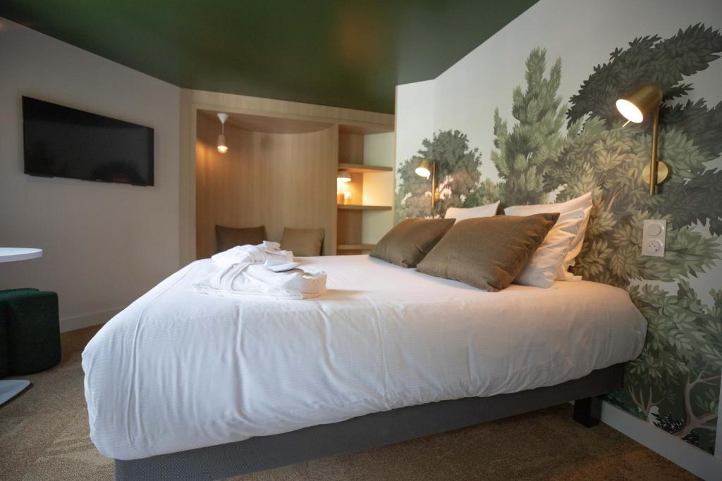 Chambre double d'hôtel avec plafond vert foncé, ornée d'un grand papier peint mural botanique en guise de tête de lit à droite avec applique laiton, literie blanche avec peignoirs pliés déposés sur le lit, téléviseur mural et alcôve éclairée avec étagères en arrière-plan à gauche, un cadre apaisant pour un séminaire bien-être.