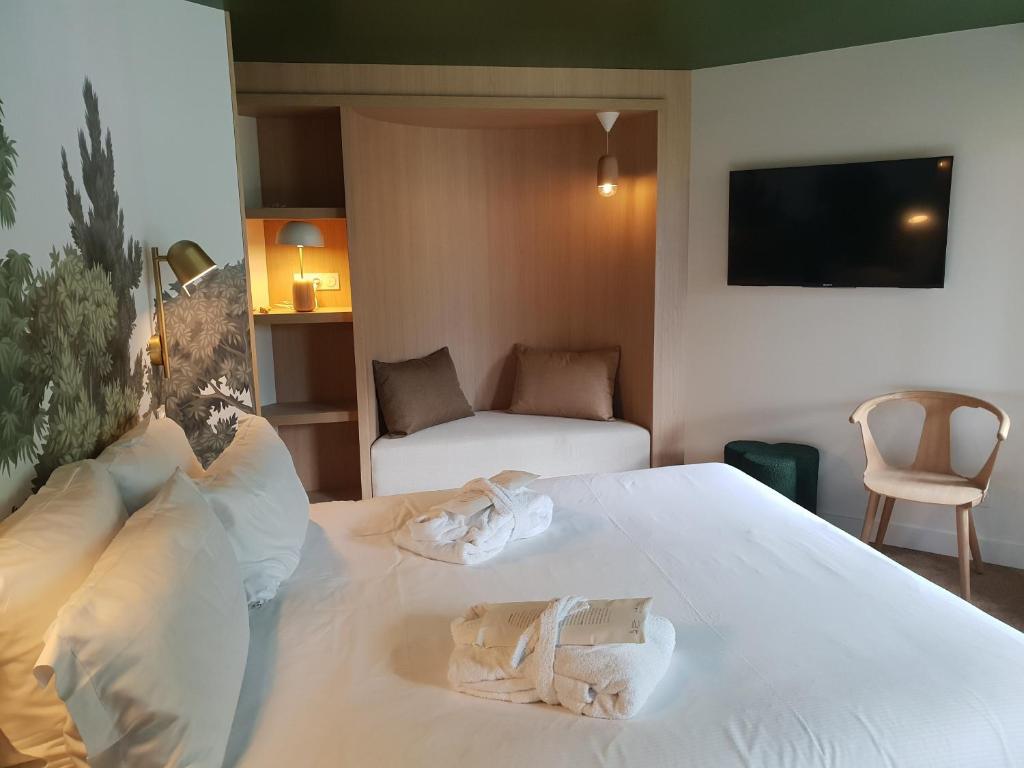 Chambre double d'hôtel avec plafond vert foncé et papier peint mural botanique à gauche, literie blanche avec deux peignoirs pliés sur le lit, une alcôve en bois éclairée avec canapé-lit et étagères au centre en arrière-plan, téléviseur mural et chaise en bois clair avec pouf vert à droite, un espace accueillant pour un séminaire bien-être.