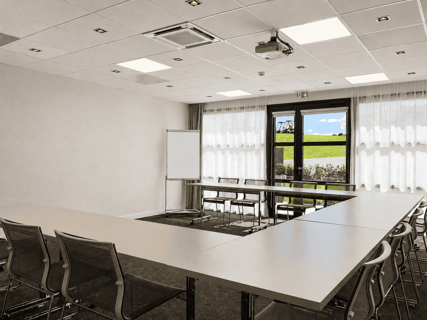 Seminar room in Saint-Quentin-en-Yvelines overlooking Le Golf National and electric golf carts, with white U-shaped tables and grey carpet.
