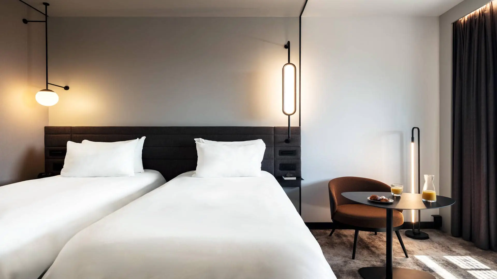 Double bed in twin configuration, with a table and chair beside it, featuring fruit juice and pastries.