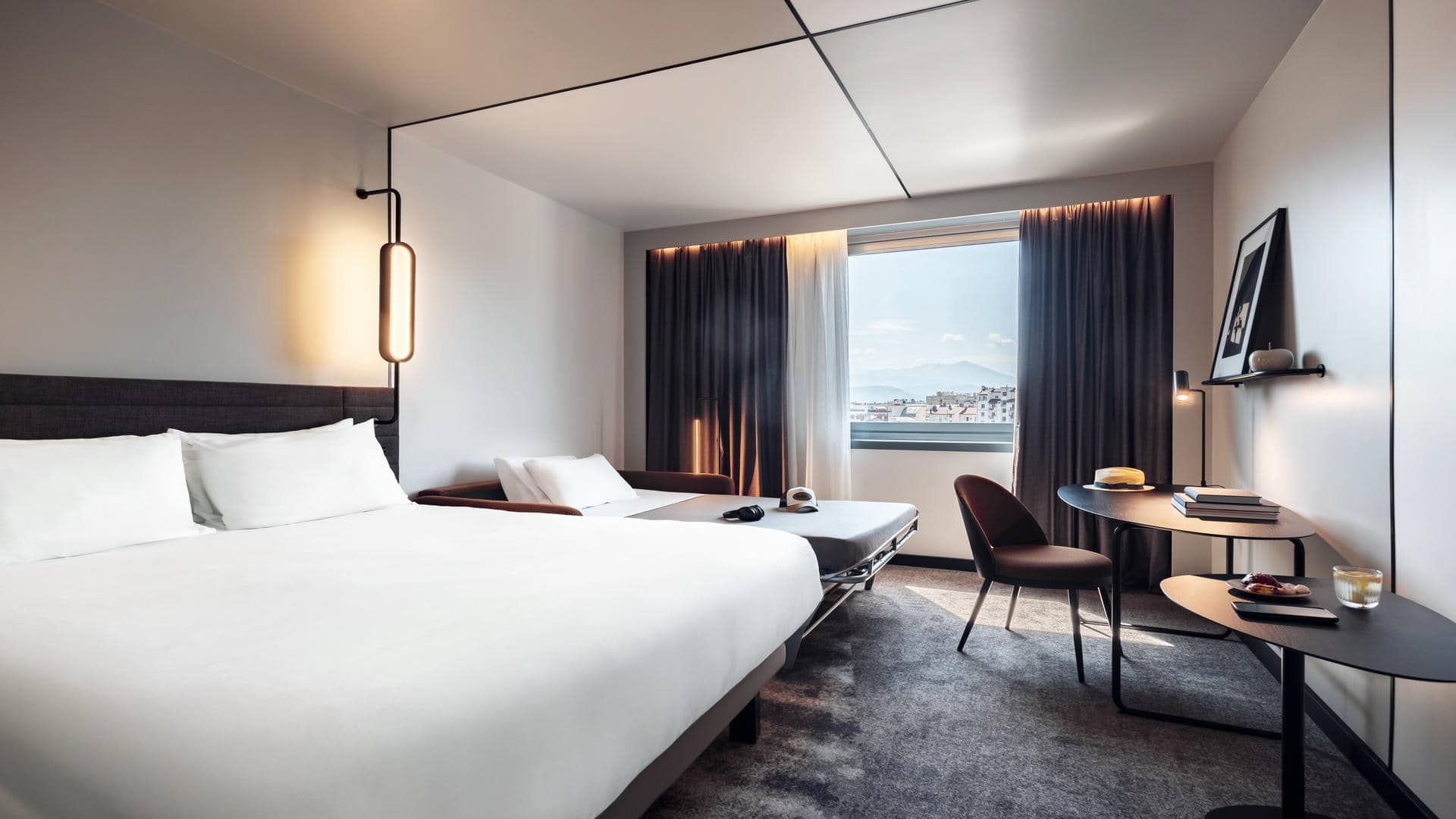 Large double bed with an open double sofa bed beside it, facing the desk, and a large window on the left overlooking the city of Grenoble.