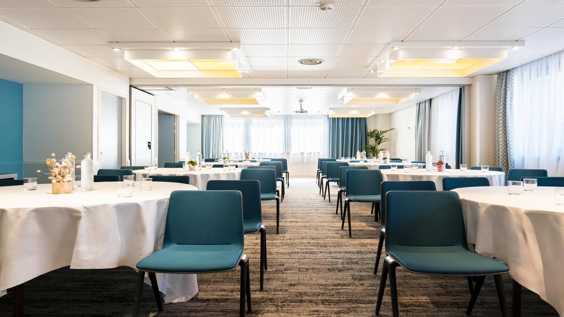 en::Reception venue set up in banquet style, with round tables, floral centrepieces and grey, turquoise, green and white tones. fr::Lieu de réception présenté en banquet, avec tables rondes, centres de table fleuris et tonalités grises, turquoise, vertes et blanches.