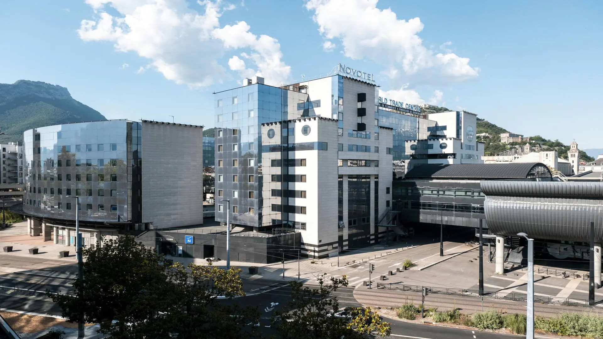 Seminar hotel in Grenoble, shown in daylight under a blue sky, with an exterior view of the building adjoining the CCI and the World Trade Center, just a short walk from the SNCF train station.