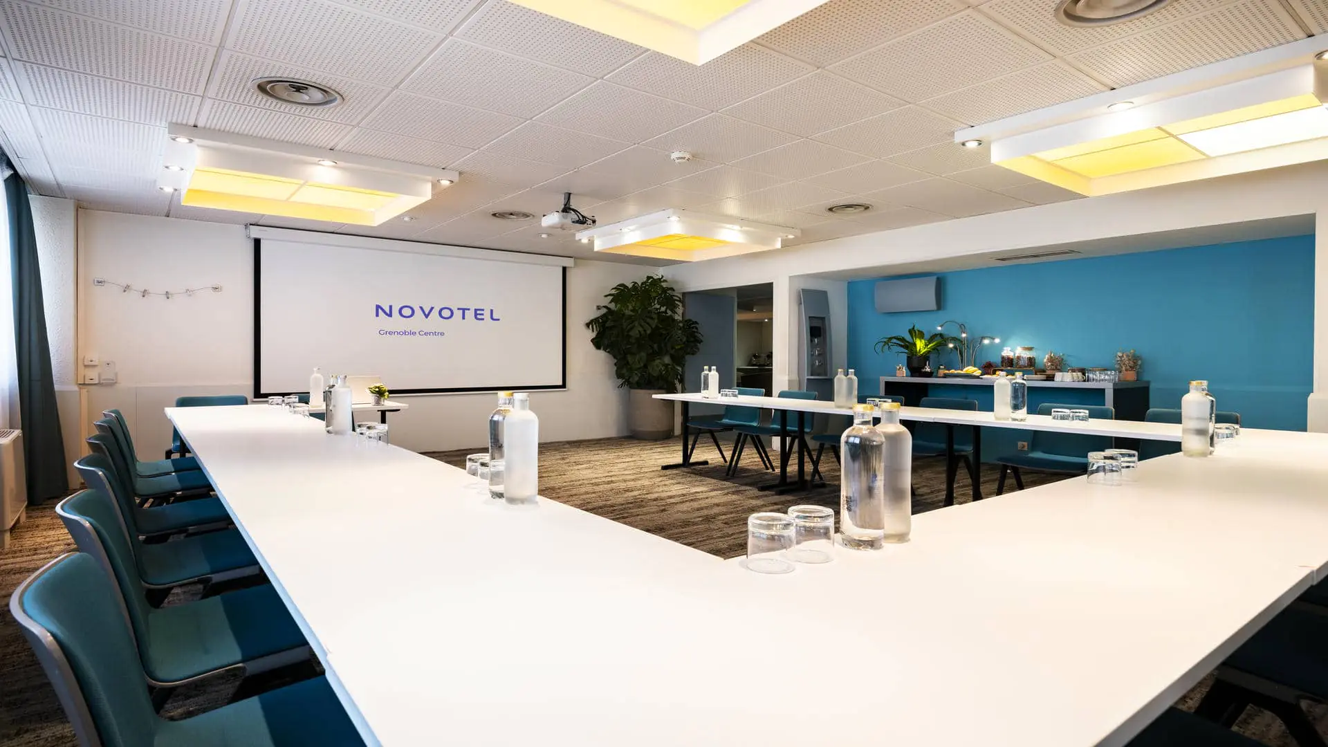 en::Meeting room with blue and white walls, grey carpet and U-shaped setup facing a screen, in a seminar venue in Grenoble. fr::Salle de réunion avec murs bleu et blanc, moquette grise et configuration en U face à un écran, dans un lieu de séminaire à Grenoble.