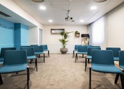 Air-conditioned training room in Grenoble, equipped with a projection screen, featuring blue and grey chairs, a wall in matching shades of blue, a large window, and soft-toned décor. fr: Salle de formation à louer au Novotel Grenoble, équipée d’un rétroprojecteur, avec des chaises bleues et grises, un mur dans des tons de bleu assortis, une grande fenêtre et une décoration aux tons doux.