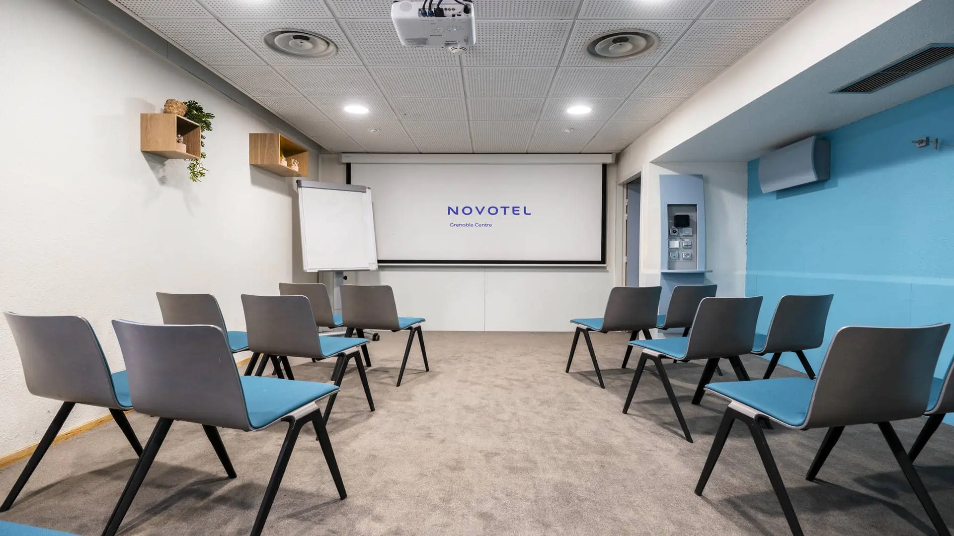 Air-conditioned seminar room in Grenoble, equipped with a projection screen, with blue and grey chairs and a wall in matching shades of blue.