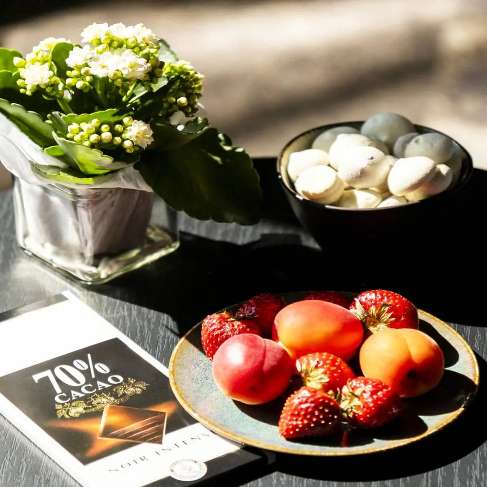 Bouquet of flowers, anise cake, bowl of strawberries and apricots, and dark chocolate, illustrating a personalized welcome that can be arranged via the Atypiic platform.