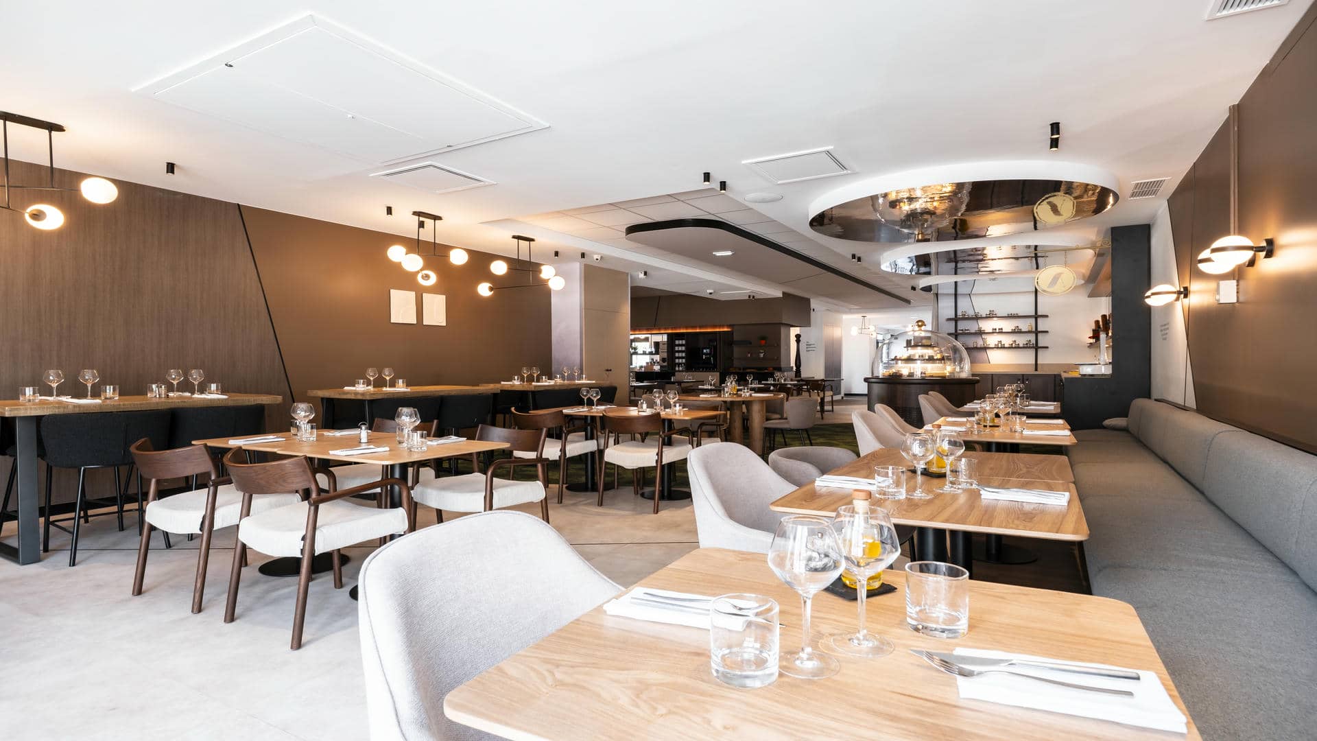 The seminar restaurant is photographed from the street-side entrance towards the back of the room, with square wooden tables and higher tables, along with sofa seating and fabric chairs.