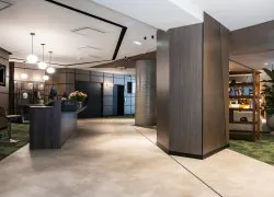 en::Reception area of the Novotel Grenoble Centre, with designer brown desks on the left, access to the lifts in the background and a large lobby opening onto the bar behind tall columns on the right. fr::Réception du Novotel Grenoble Centre avec desks marron design à gauche, accès aux ascenseurs au fond et grand lobby ouvert sur le bar derrière de hautes colonnes à droite.