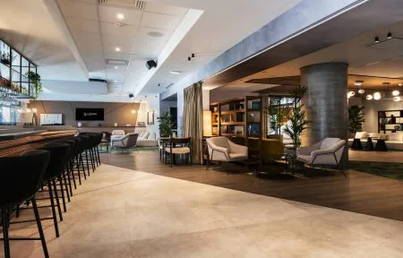 Large wooden bar counter with perfectly aligned high chairs, cinema lounge in the background and two bookcase areas in a seminar venue in Grenoble.