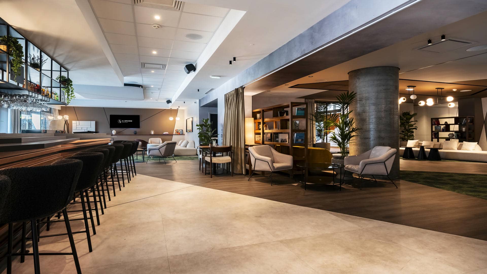 Large wooden bar counter with perfectly aligned high chairs, cinema lounge in the background and two bookcase areas in a seminar venue in Grenoble.