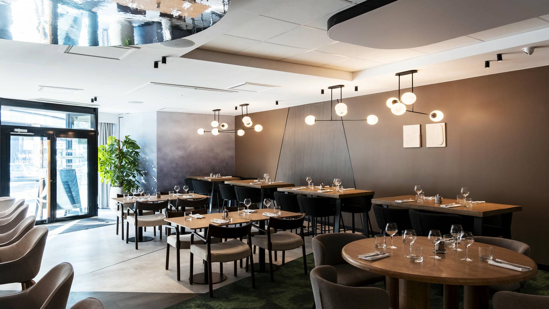 The seminar restaurant features a wood-panelled wall, tiled flooring and green carpet, with square tables, round tables and communal tables alternating throughout the space.