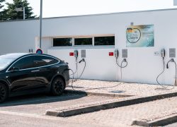 en::Parking area with an electric car charging, featuring Novotel Chartres signage. fr::Parking avec voiture électrique en charge et affichage Novotel Chartres.